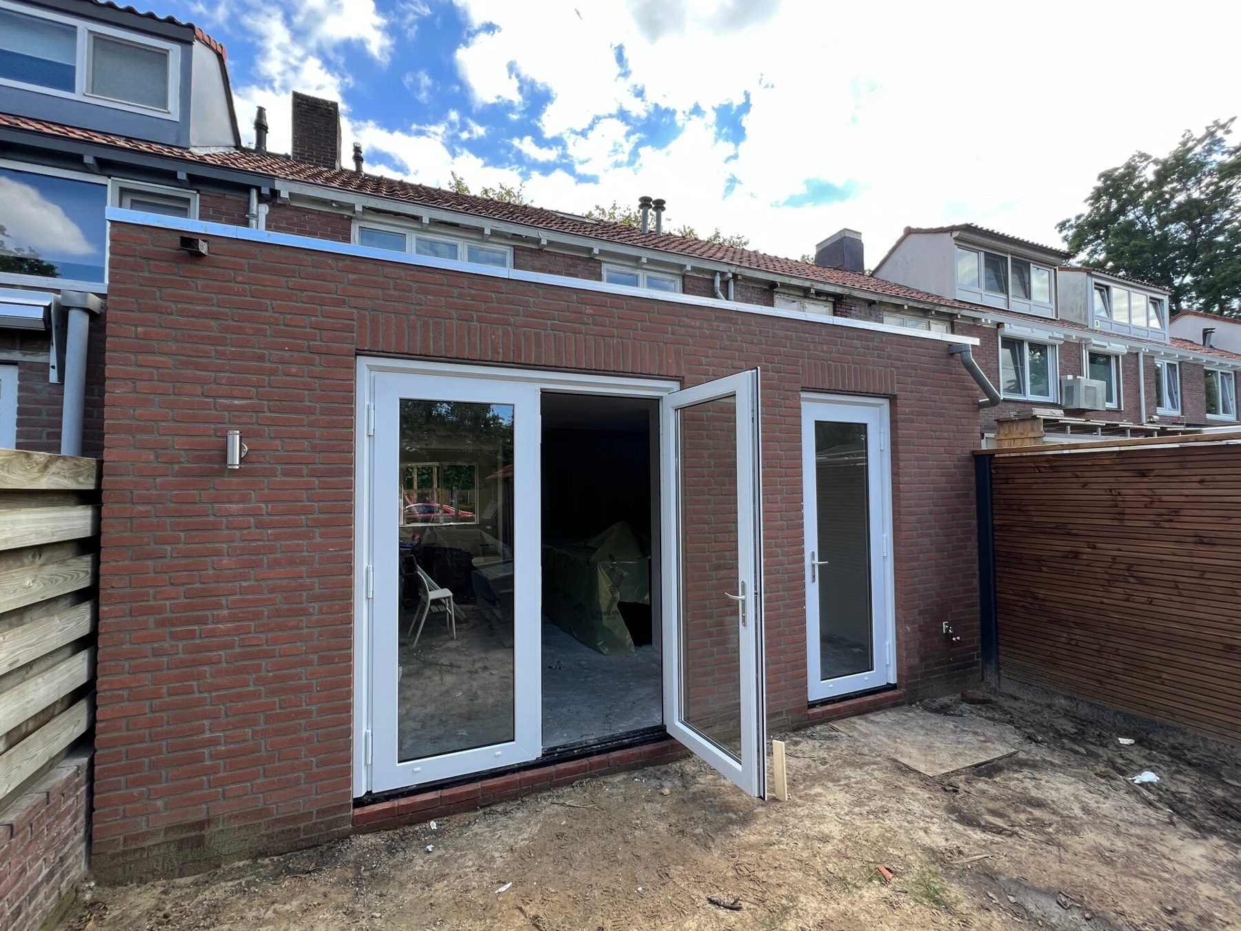 Nieuwe aanbouw in rode baksteen met openslaande witte tuindeuren, aan de achterzijde van een rijwoning
