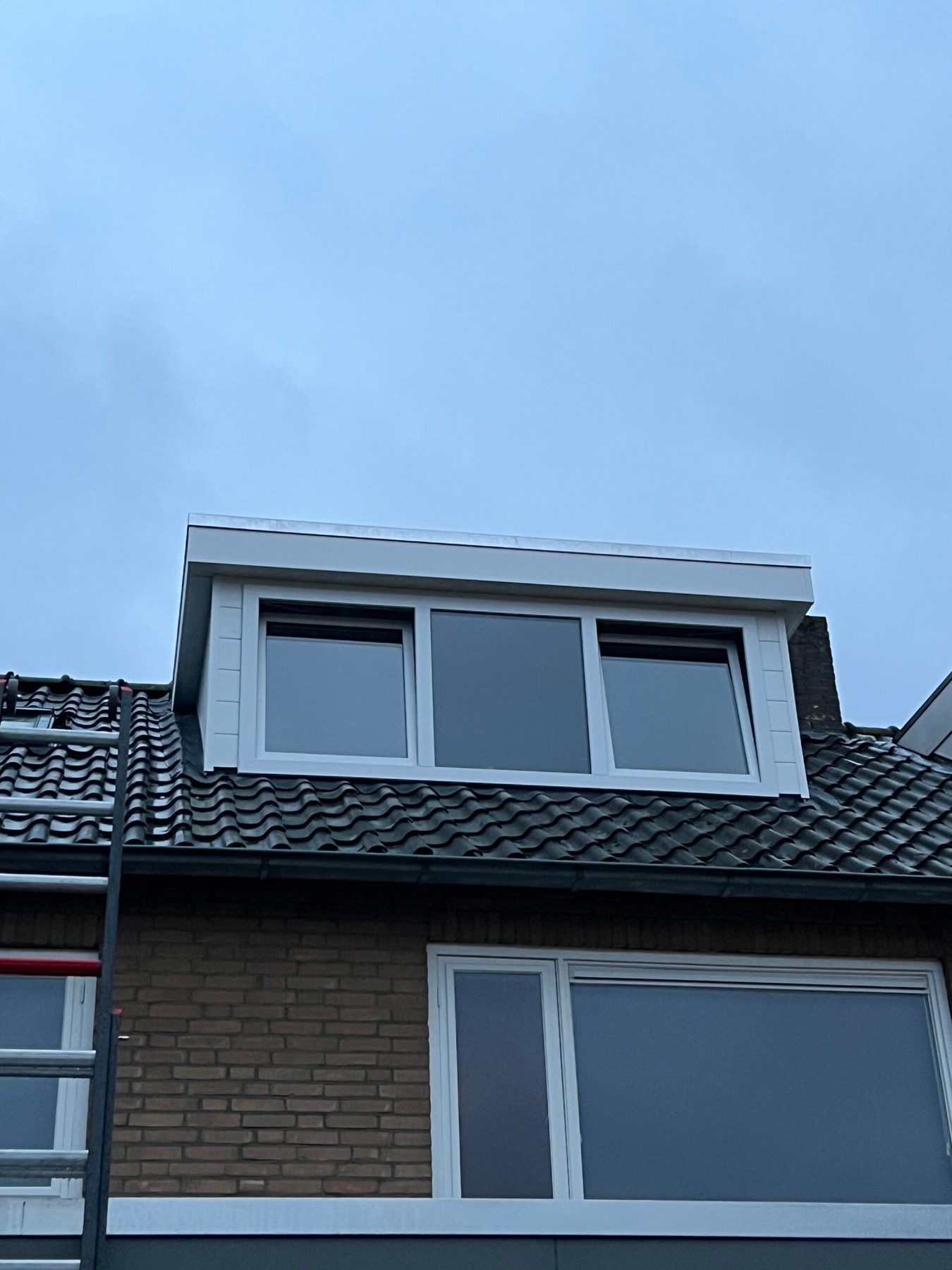 Witte kunststof dakkapel met drie ramen op een pannendak
