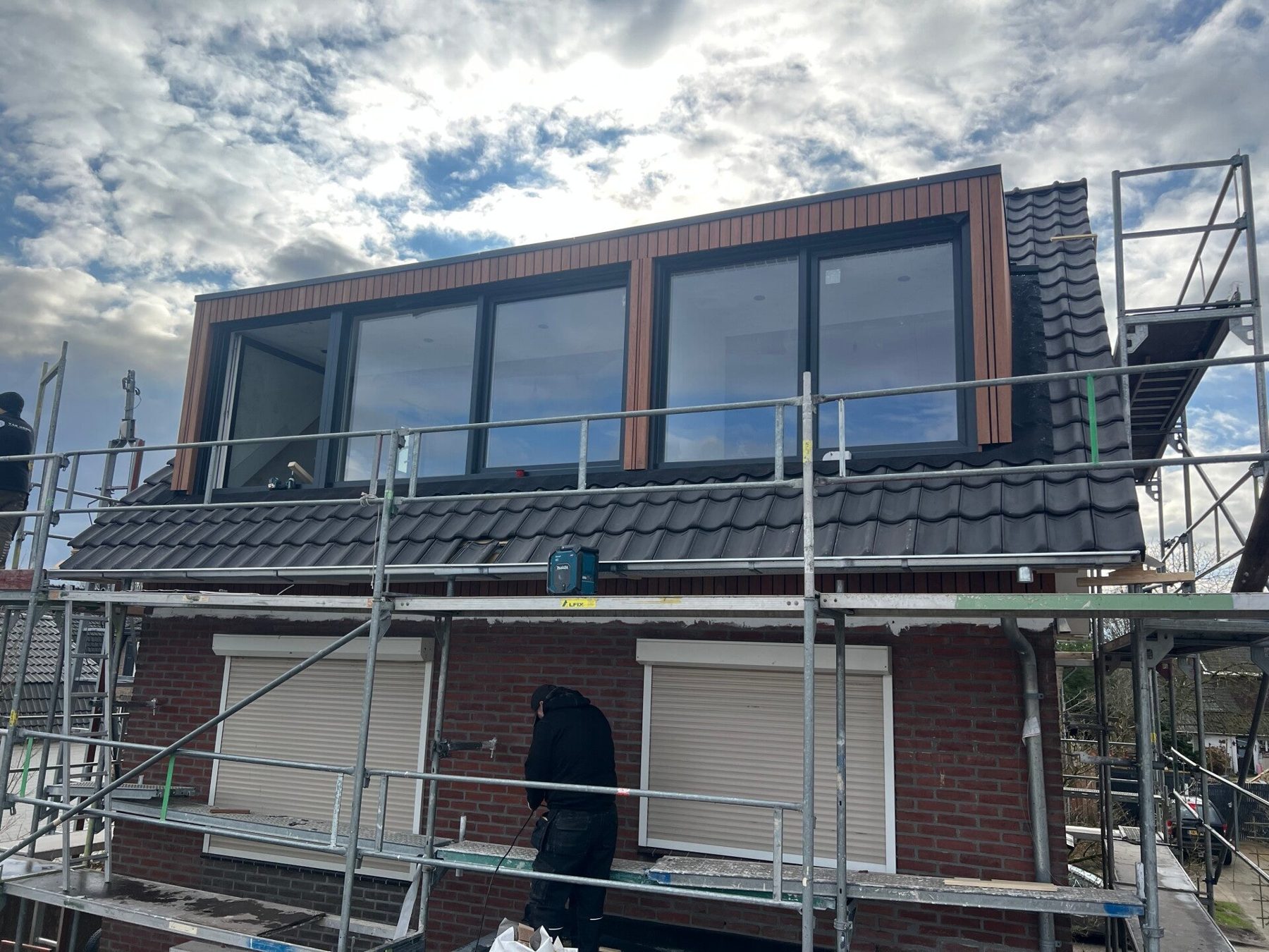 Nieuwe dakopbouw met brede raampartij en antracieten dakpannen, in de steigers op een rijwoning